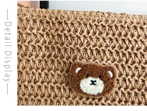 Gros plan détaillé du sac clutch en paille tissée avec un joli patch de broderie d'ours en peluche.
