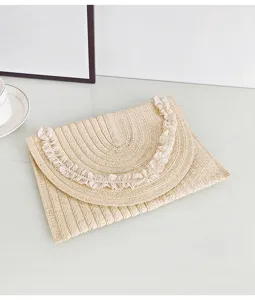 Nahaufnahme einer beigen Stroh-Karten-Clutch mit zartem weißem Spitzenbesatz für die Sommermode.