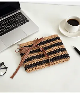 Nahaufnahme der gewebten Stroh-Clutch mit schwarzen Streifen und brauner Schleife am Tisch.