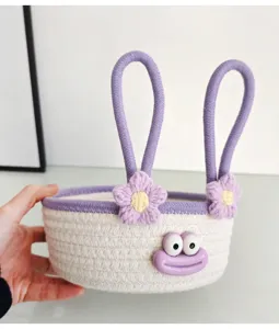Cute cotton rope storage basket close-up with purple handles, crochet flowers, and funny cartoon face.