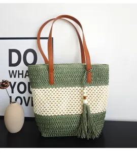 Nahaufnahme der hohlen Strohtasche mit braunen Ledergriffen und schickem Quastenanhänger.