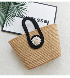 Nahaufnahme der geflochtenen Strohtasche mit schwarzen Griffen und eleganter Perlenbesatz.