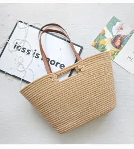 Detailed view of casual woven straw tote bag with brown leather handles for summer beach.