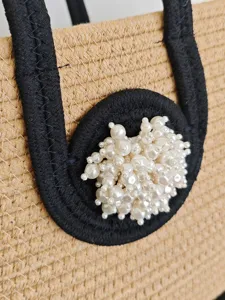 Gewebte Stroh Handtasche mit schwarzen Kontrastgriffen und eleganter Perlenbesatz Dekoration Strand.