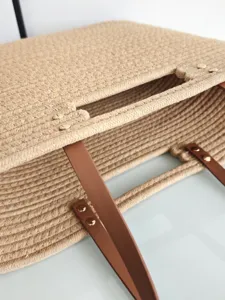 Woven straw tote bag with brown leather handles and metal rivets for casual beach vacation.