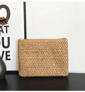 Vue détaillée de la pochette en paille tressée, montrant la texture artisanale et la fermeture.