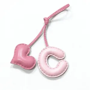 Vista detallada del colgante de bolso de cuero rosa con corazón y letra C bien cosido.