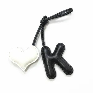 Handgefertigter Leder-Buchstabe K und weißer Herz-Taschenanhänger mit feinen Nähten.