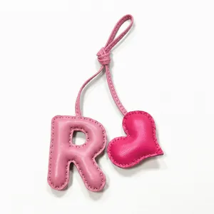 Ciondolo borsa artigianale in pelle rosa con lettera R e cuore, elegante accessorio donna.