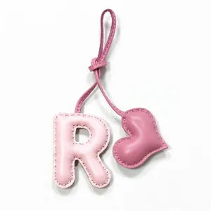 Dettaglio del ciondolo per borsa in pelle rosa con lettera R e cuore, cuciture e laccetto.