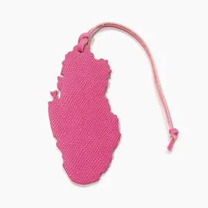 Détail de charm de sac en cuir rose en forme de carte du Qatar, texture fine et lanière assortie.