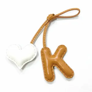 Detaillierte Nahaufnahme des handgefertigten Leder-Buchstaben-K und Herz-Taschenanhängers.