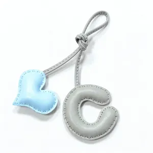 Primer plano colgante bolso corazón de cuero letra C, costura a mano, accesorio elegante.