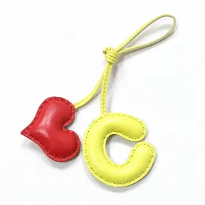 Detalle del colgante de bolso de cuero letra C y corazón rojo hecho a mano con costuras finas.