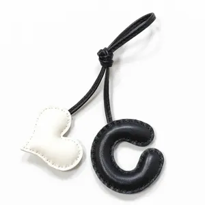 Vista detallada del colgante hecho a mano de cuero negro y blanco con letra C y corazón.