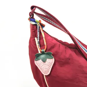 Red nylon shoulder bag detail featuring colorful twilly ribbon and leather strawberry keychain charm.