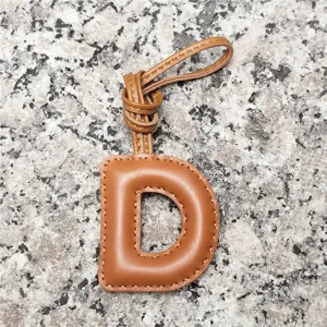 Close-up detail of the light brown lambskin letter D bag charm showing stitching texture.