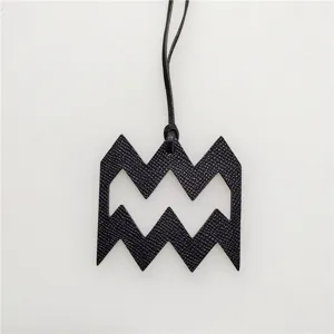 Black leather zodiac symbol pendant detail showing fine textured grain and hanging cord.