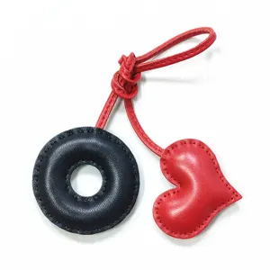 Handmade leather bag charm detail with black donut ring and red heart pendant design.