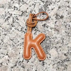 Detailed close-up shot of the brown leather initial letter K pendant with stitched edge texture.