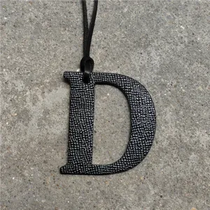 Black textured leather letter D bag charm with leather cord, stylish accessory pendant.