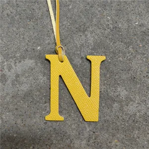 Close-up of yellow leather letter N bag charm pendant showing fine textured leather surface and strap.
