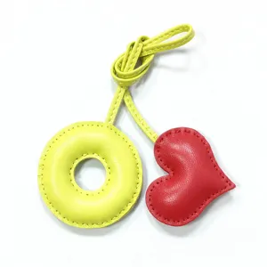 Handmade leather charm detail featuring a yellow O-shaped ring and red puffy heart pendant.