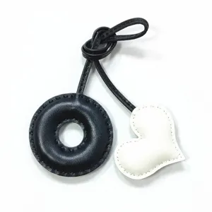 Handmade leather bag charm featuring a black donut ring and white heart pendant for purse decor.