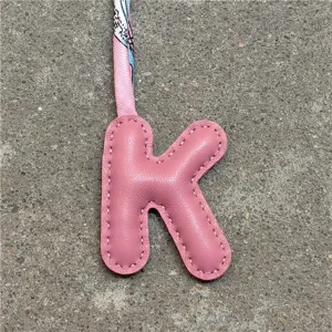 Nahaufnahme eines rosafarbenen Leder K Buchstaben Taschenanhängers mit schickem Twilly Seidenband.