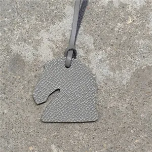 Vue détaillée d'un mini charm's de sac tête de cheval en cuir gris avec fine texture.