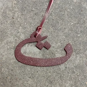 Close-up view of a maroon textured leather Arabic letter bag charm pendant detail.