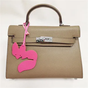 Elegant taupe top handle handbag with pink fox leather charm and secure turn-lock closure.