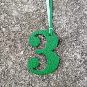 Close-up detail shot of a green leather number 3 charm with a light blue hanging cord.
