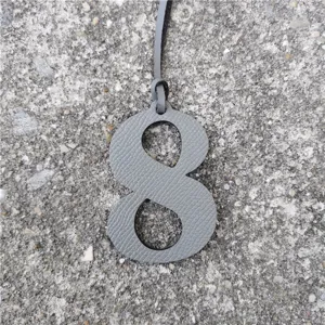 Detailed shot of a gray leather number 8 bag charm with fine strap on textured stone ground.
