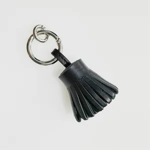 Detalle de llavero de borla de cuero negro, mini dije de bolso con flecos y anillo metálico.