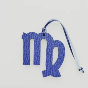 Detailed closeup view of a blue textured leather Virgo zodiac sign bag charm pendant.