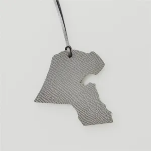 Gros plan détaillé du pendentif de sac en cuir gris représentant la carte de l'état du Koweït.