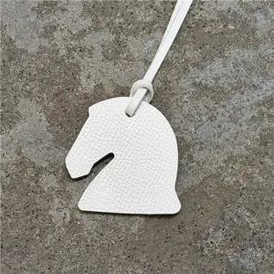 Détail de breloque de sac tête de cheval en cuir blanc, design épuré avec lanière assortie.