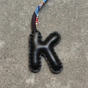 Detailansicht des schwarzen Leder-Buchstaben-K-Taschenanhängers mit buntem Seidenband.