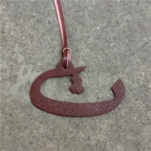 Detailed shot of a burgundy leather Arabic letter bag charm pendant with a strap.