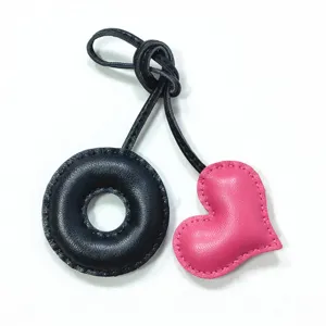 Handmade leather bag charm featuring a black donut ring and pink heart pendant.
