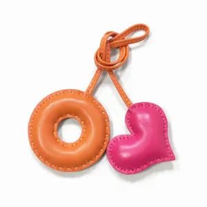 Handmade leather bag charm with donut and heart shapes, featuring elegant contrast saddle stitching.