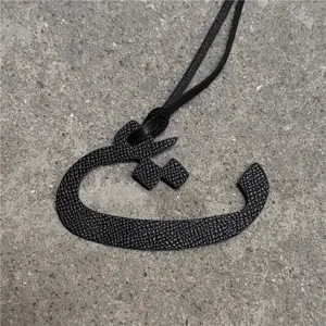 Close-up detail view of the black textured leather Arabic letter pendant bag charm accessory.