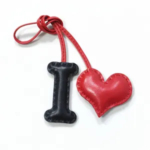 Close-up of handmade leather letter I and red heart bag charm pendant detail shot.