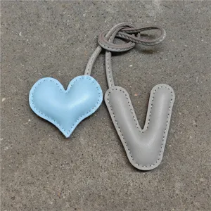 Vista detallada de colgante de bolso de cuero hecho a mano con letra V y corazón.