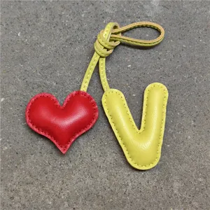 Vista detallada del dije de bolso de cuero hecho a mano con corazón y letra V con costura.
