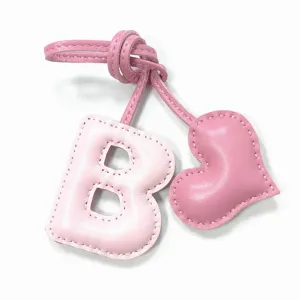 Detalle de dije de bolso letra B y corazón de cuero rosa, accesorio hecho a mano.