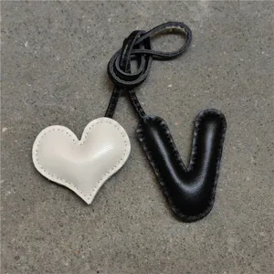 Colgante de bolso de cuero artesanal con corazón blanco acolchado y letra V negra elegante.