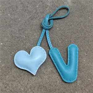 Colgante de bolso de cuero hecho a mano con corazón y letra V, costuras y tira de nudo.