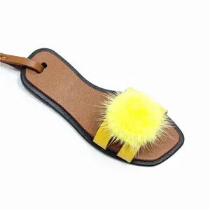 Nahaufnahme des Miniatur Leder Sandalen Taschenanhängers mit flauschigem gelben Nerzpelzball.